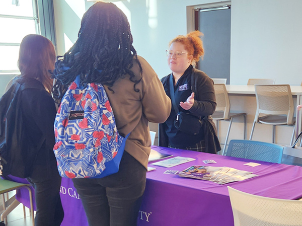 Girl wearing backpack with friend talking to a college rep at the college fair